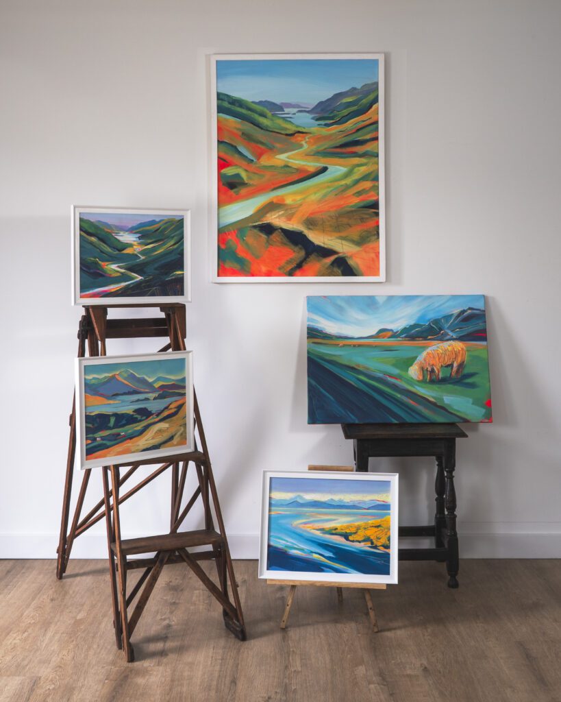 Colourful landscape paintings displayed on easels indoors